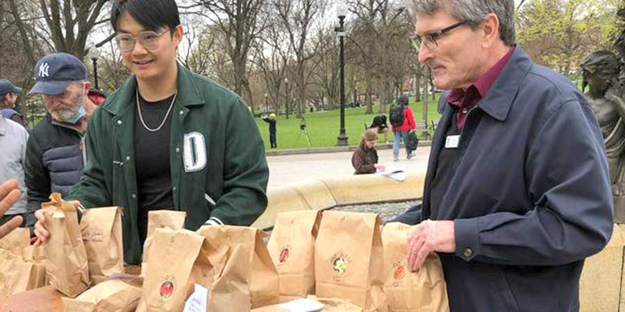 Two people on Boston common distributing food from paper bags